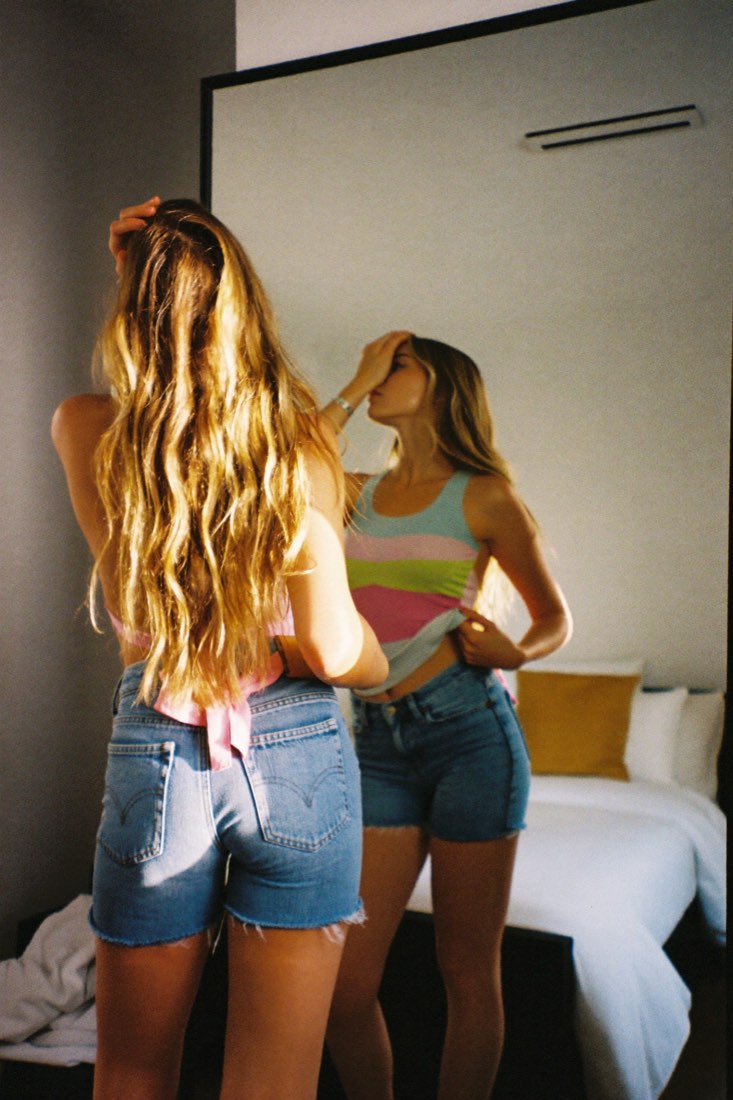 A young blonde woman checking her outfit in a full-length mirror in golden light