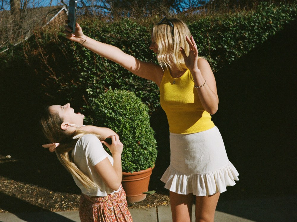 Two friends filming a video on a phone in a sunny backyard